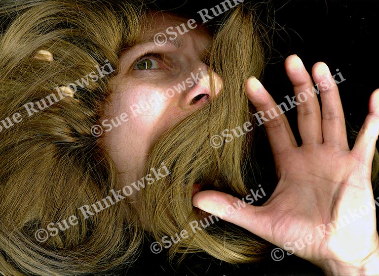 A close-up image of a woman’s face and hands pressed flat against a glass surface, creating a distorted effect. Her expression is one of alarm or distress, with wide eyes and an open mouth as if shouting or gasping. Her long, light brown hair fans out around her face, contributing to the sense of entrapment or urgency. The image conveys a raw, emotional intensity and a sense of being trapped or silenced.