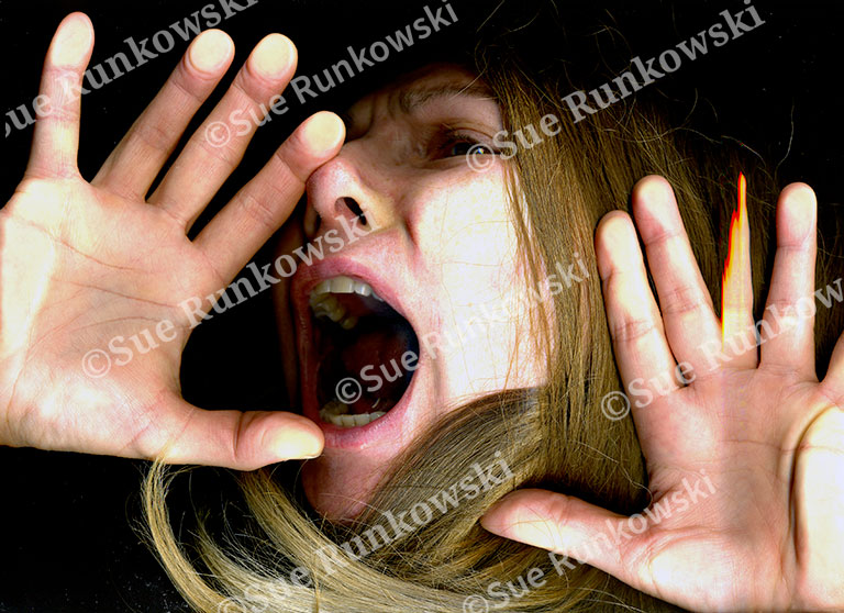 A close-up image of a woman’s face and hands pressed flat against a glass surface, creating a distorted effect. Her expression is one of alarm or distress, with wide eyes and an open mouth as if shouting or gasping. Her long, light brown hair fans out around her face, contributing to the sense of entrapment or urgency. The image conveys a raw, emotional intensity and a sense of being trapped or silenced.