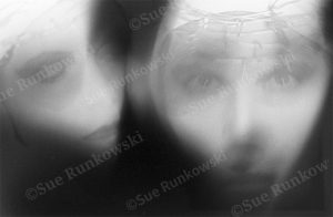 Abstract black-and-white digital photo with blurred, double-exposed faces with stitched details across the forehead.