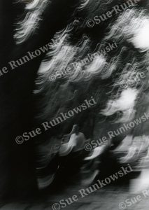 Black-and-white photograph capturing a blurred meditative, bodhisattva-like figure with streaks of light in NYC.