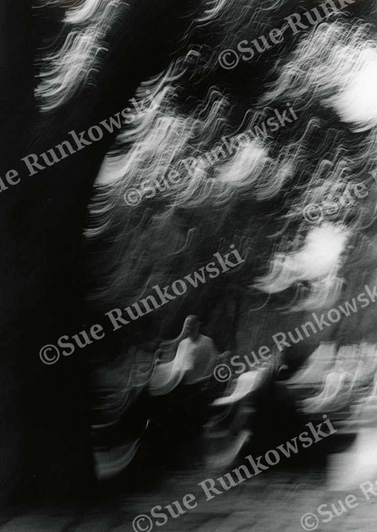 Black-and-white photograph capturing a blurred meditative, bodhisattva-like figure with streaks of light in NYC.