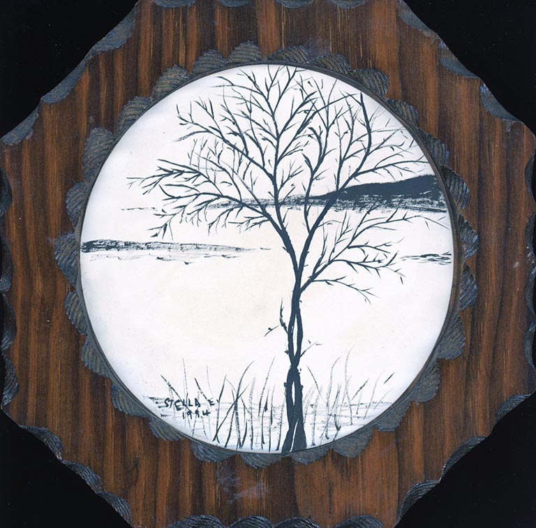 A pen & ink drawing of a tree by the river in a square wooden frame.