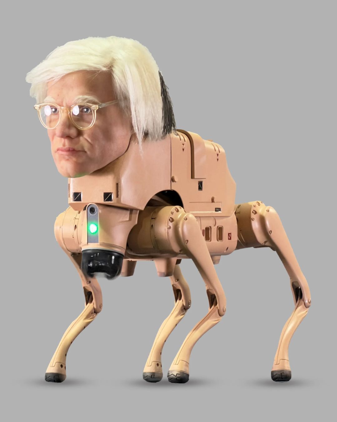 A surreal digital artwork depicting a four-legged robotic dog with a beige, mechanical body and jointed legs, topped with a human-like head featuring pale skin, short white hair, and clear-framed glasses. A small green light glows on the front of the robot’s body against a plain gray background.