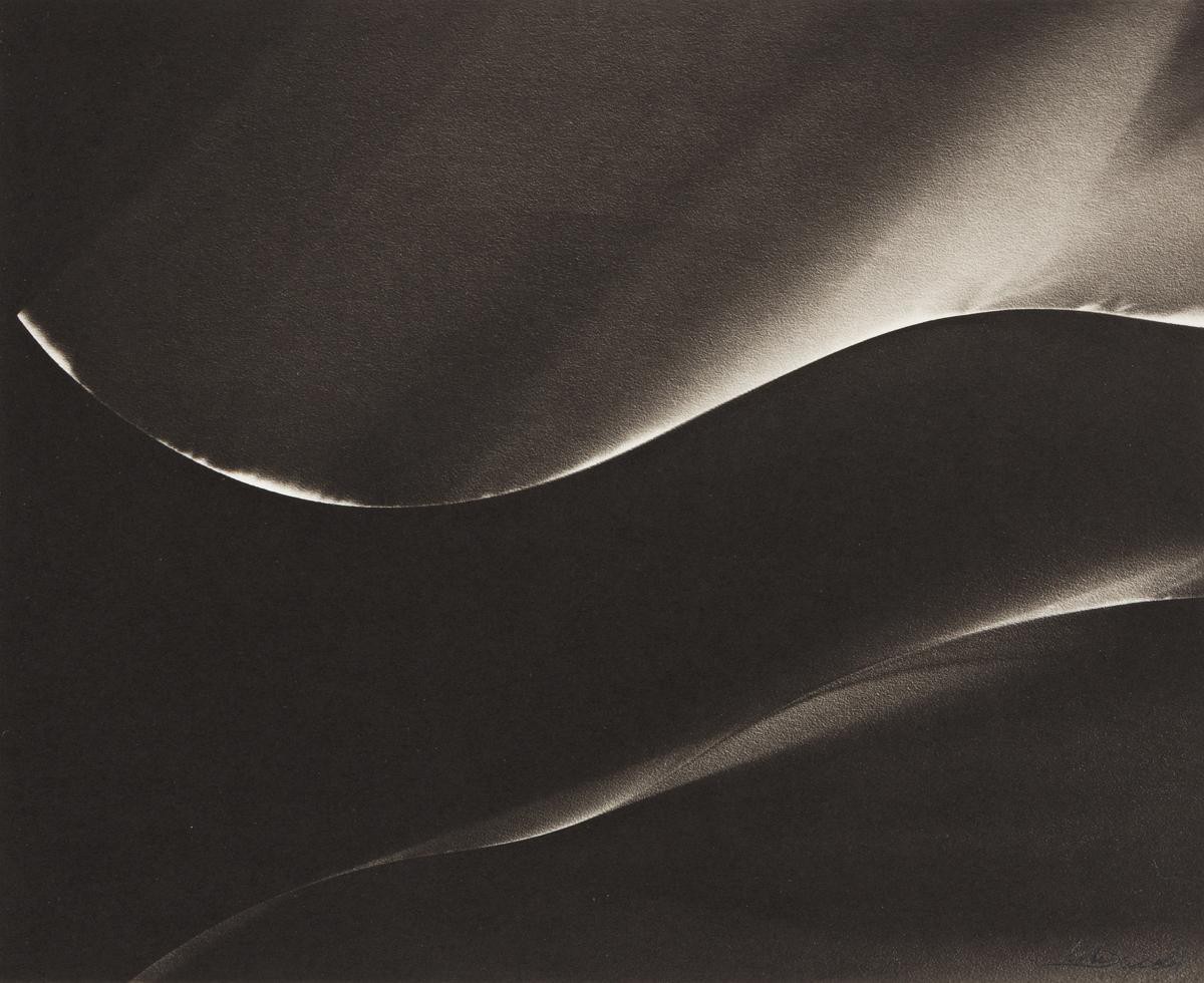 An abstract black-and-white photograph featuring softly curved, wave-like forms illuminated by delicate highlights against a deep dark background. The flowing contours resemble sculpted fabric, rolling dunes, or the smooth curves of the human body, creating a quiet, atmospheric composition with a surreal and tactile quality.